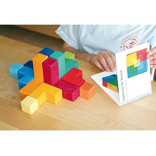 Een kind houdt een Grimm's voorbeeldboekje vast met een geometrisch puzzelpatroon, naast een deels gebouwde kleurrijke houten puzzel.