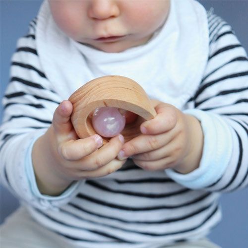 Een baby houdt de Grimm's houten rammelaar-bijtring met rozenkwarts vast.