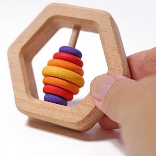 Een hand houdt de Grimm's houten zeshoekige rammelaar met regenboogkleurige ringen vast.