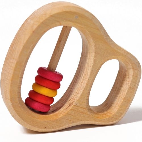 Grimm's houten rammelaar en bijtring met rode en gele ringetjes, schuin van bovenaf gefotografeerd.