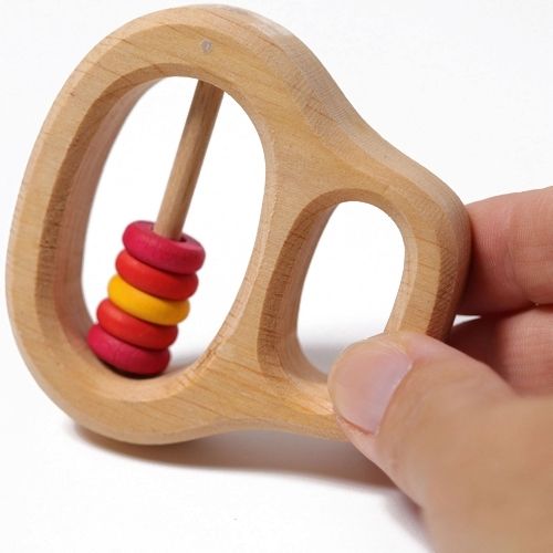 Een hand houdt de Grimm's houten rammelaar en bijtring vast, met de rode en gele ringetjes zichtbaar.