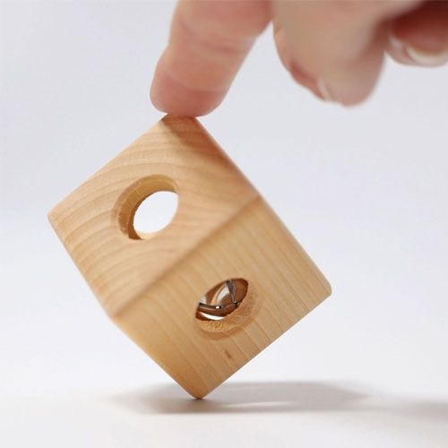 Een hand houdt de grimm's houten rammelaar kubus vast, waarbij het belletje binnenin zichtbaar is.