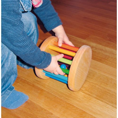Een kind speelt met de Grimm's houten regenboog rammelaar op een houten vloer.