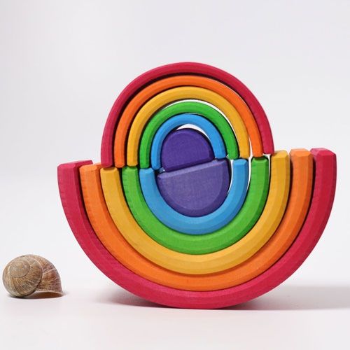 Grimm's houten regenboog stapelspeelgoed in een cirkelvormige opstelling, naast een slakkenhuisje voor schaal.