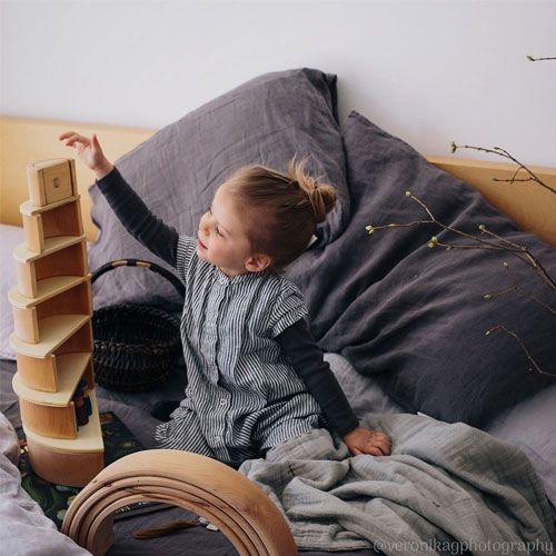 Een kind zit op bed en speelt met een grimm's houten stapeltoren van bogen.
