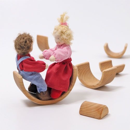Twee poppen spelen op een houten boog die als wip wordt gebruikt, met andere houten bogen op de achtergrond.