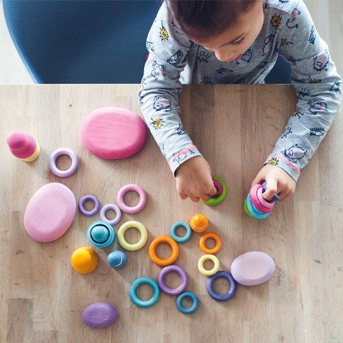 Een kind speelt aan tafel met grimm's pastelkleurige houten ringen en andere vormen.