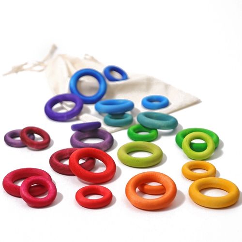 grimm's regenboog houten ringen in verschillende maten, verspreid op een witte ondergrond met een stoffen zak.