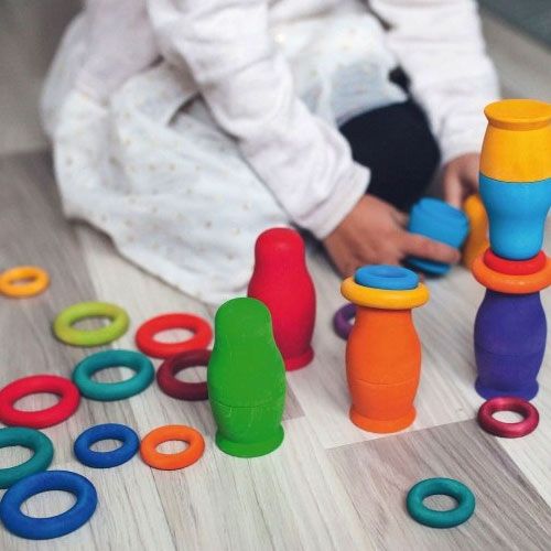 Een kind speelt met grimm's regenboog houten ringen en figuren op een houten vloer.
