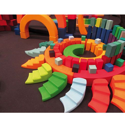 Grimm's houten bouwspeelgoed met wenteltrappen en andere blokken in regenboogkleuren, op een donkere ondergrond.