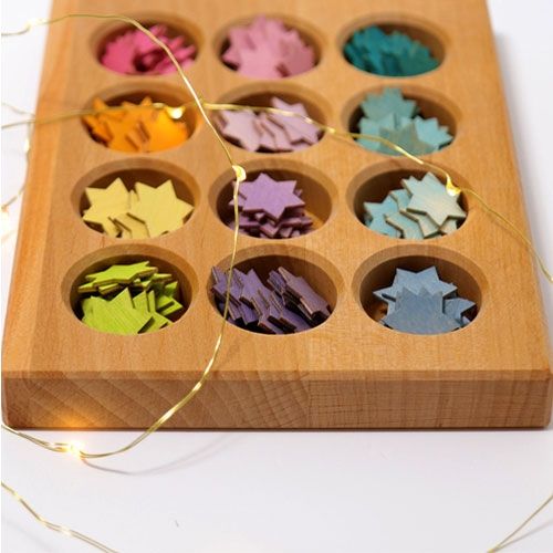 Bovenaanzicht van het grimm's houten sorteerbord met twaalf vakjes gevuld met pastelkleurige houten sterren, omringd door een lichtsnoer.