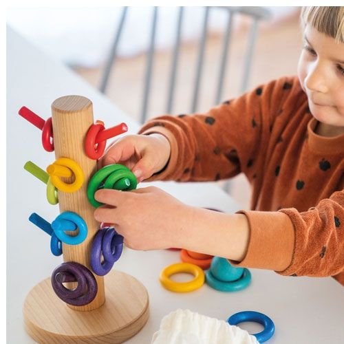 Een kind speelt met de Grimm's houten sorteerkapstok en plaatst een groene ring op een pin.