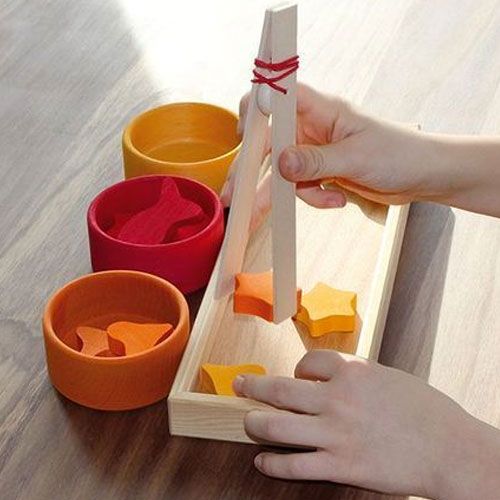 Een kind gebruikt een houten pincet om een oranje ster uit een sorteerbakje te pakken.