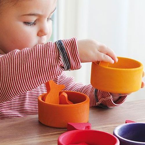 Een kind houdt een oranje houten sorteerbakje vast met houten vormen van dieren.