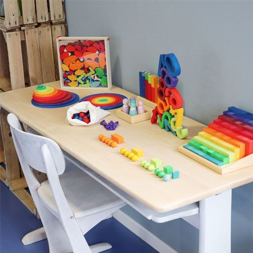 Een tafel vol grimm's houten speelgoed in regenboogkleuren, waaronder stapelcijfers, ringen en blokken.