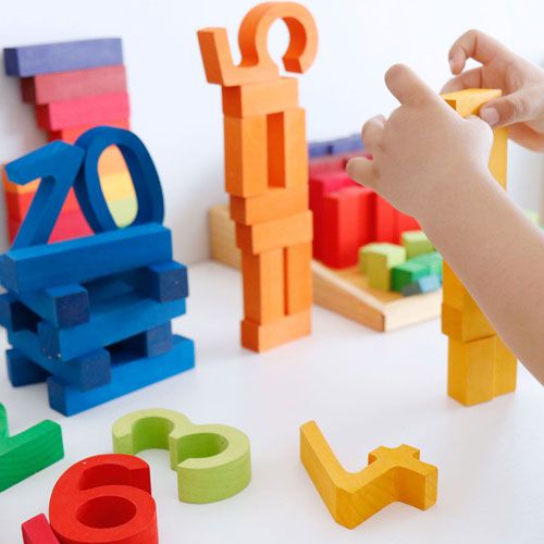Kinderhanden stapelen oranje grimm's houten cijfers, met andere kleurrijke cijfers en blokken op de achtergrond.