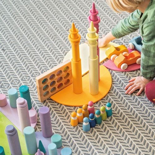 Een kind speelt met diverse grimm's houten bouwspeelgoed in pastelkleuren, waaronder stapelrollers en torens.