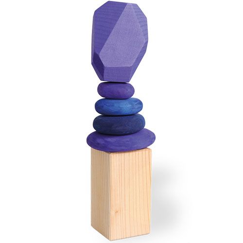 Een grimm's houten stapelset met paarse en blauwe kiezelstenen en een gefacetteerd blok, balancerend op een houten kubus.