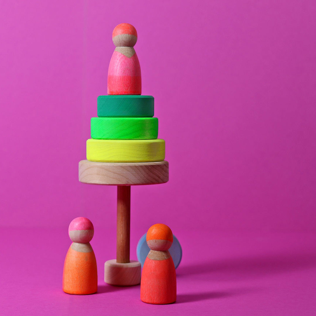 Grimm's houten stapelspeelgoed met neon groene en gele ringen en drie gekleurde houten poppetjes op een roze achtergrond.