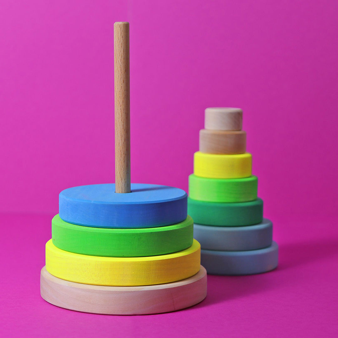 Twee Grimm's houten stapeltorens voor baby's en peuters, met veelkleurige ringen, op een roze achtergrond.