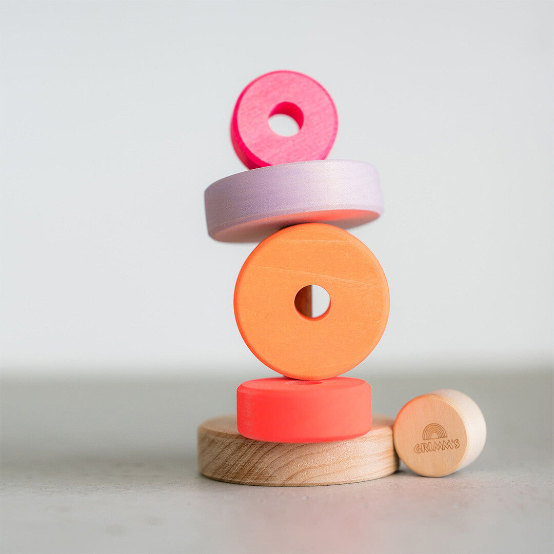 Grimm's houten stapeltoren voor baby's met neonkleurige ringen die losjes op elkaar gestapeld zijn, met het merklogo zichtbaar.