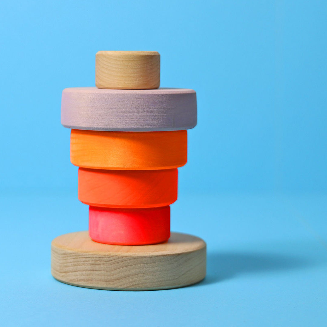 Grimm's houten stapeltoren voor baby's met neonkleurige ringen en natuurlijke houten elementen op een blauwe achtergrond.