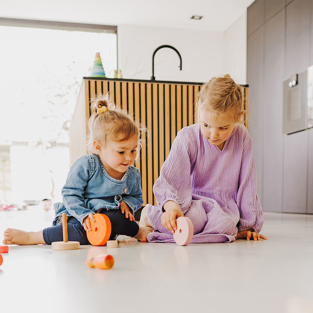 Twee kinderen spelen op de vloer met Grimm's houten stapeltorens met veelkleurige ringen.