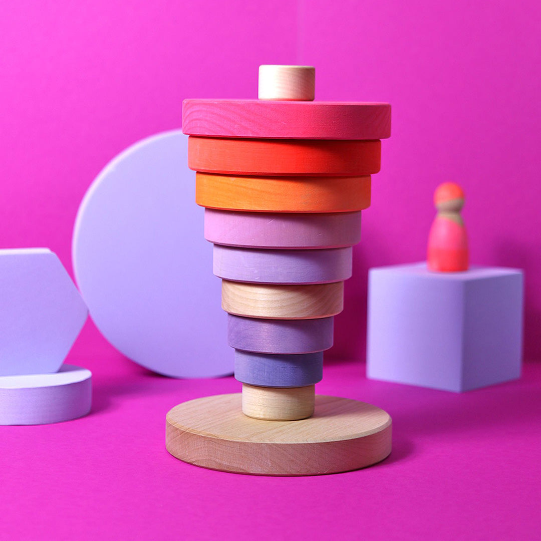 Grimm's houten stapeltoren met veelkleurige neon ringen op een roze achtergrond met geometrische vormen.
