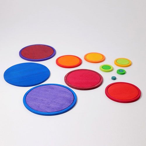 grimm's houten stapelspeelgoed met losse regenboogkleurige schijven en ringen verspreid op een witte ondergrond.