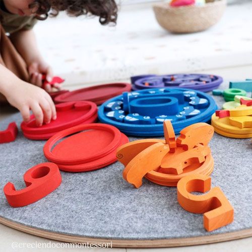 Een kind speelt met grimm's houten stapelspeelgoed en houten cijfers op een grijze speelmat.