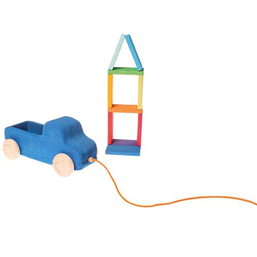 Grimm's houten trekfiguur vrachtwagen naast een toren van regenboogkleurige houten blokken.