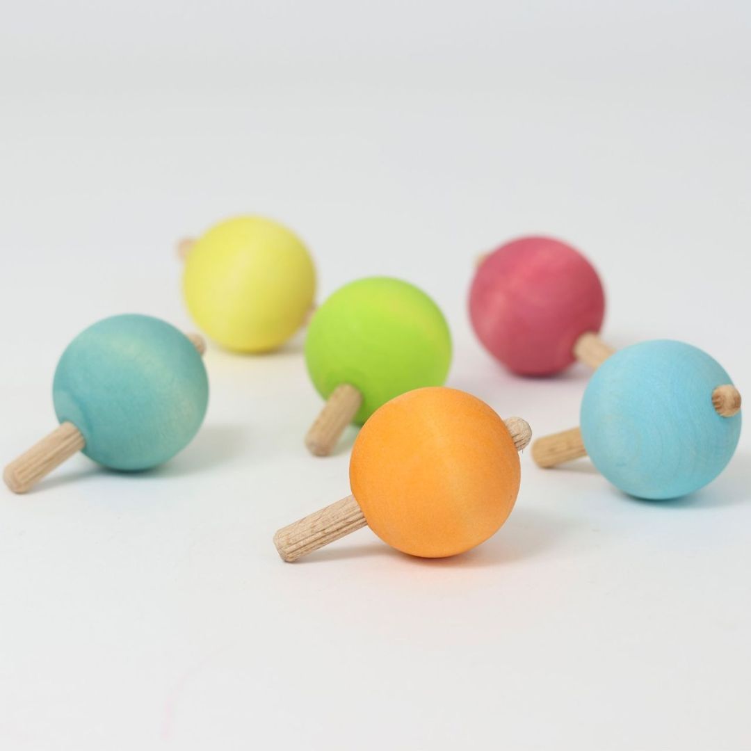 Grimm's zes houten tollen in pastelkleuren verspreid op een witte ondergrond.