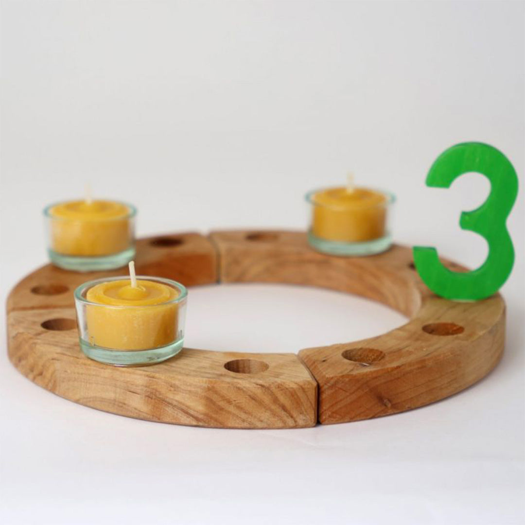Drie glazen houders met gele waxinelichtjes in een houten jaarring met een groene '3'.