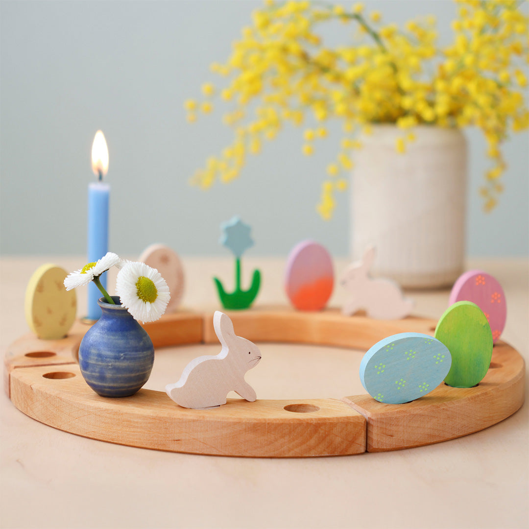 Houten paaseieren en konijntjes decoratie figuren in een houten ring met een brandende kaars en bloemen.