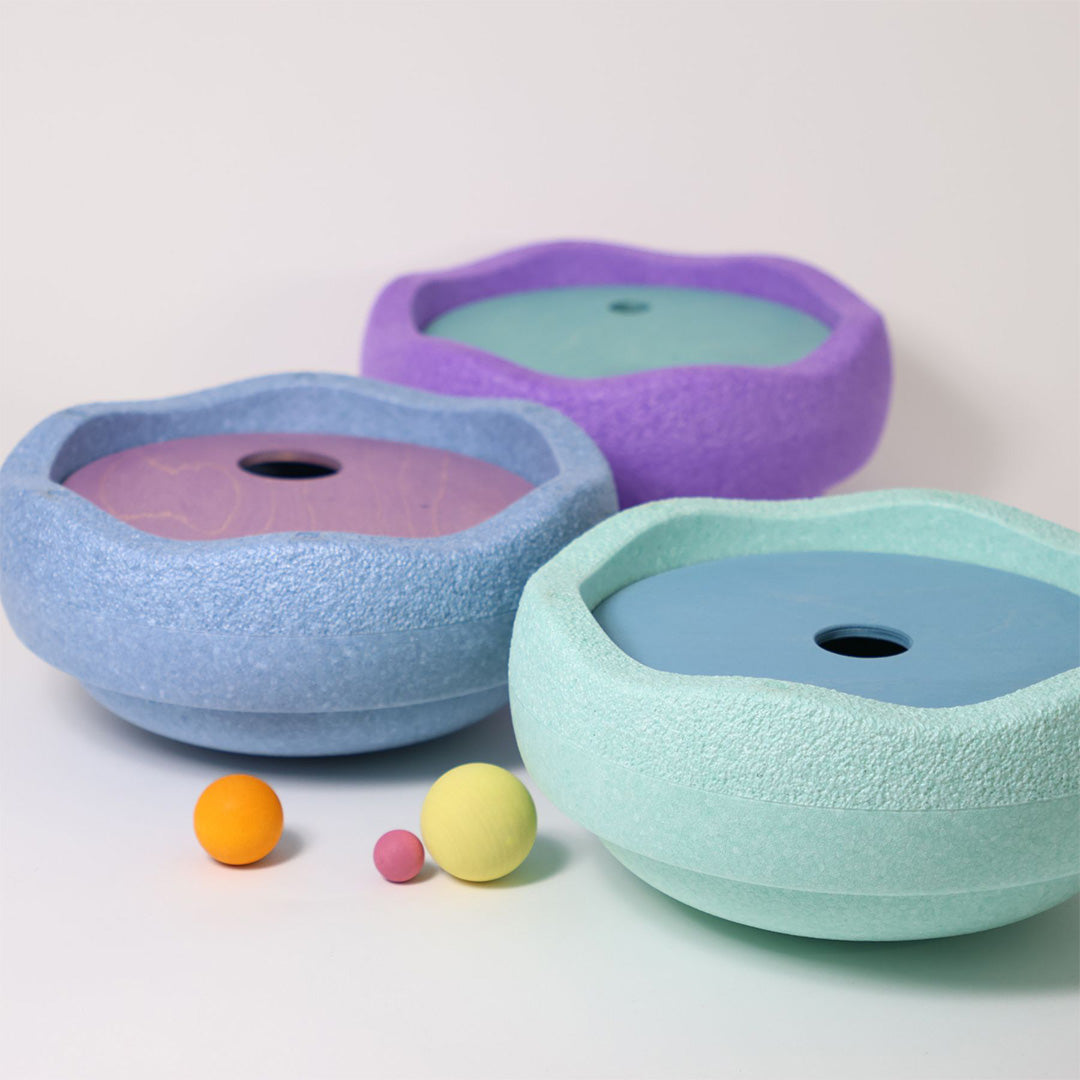 Drie grimm's rolling discs in pastelkleuren paars, lichtblauw en mintgroen, met een houten schijf in elke kom en drie kleine balletjes ervoor.