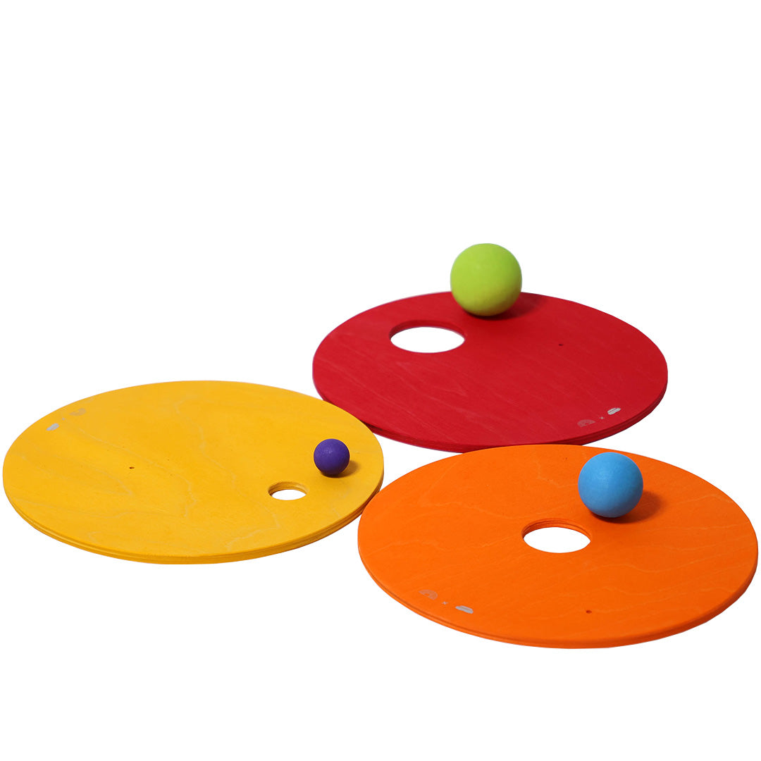 Drie grimm's houten rolling discs in rood, geel en oranje met elk een bal erop.
