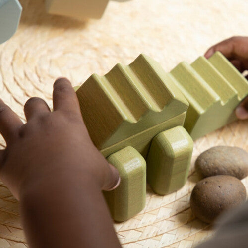 Kinderhanden spelen met een Guidecraft houten krokodil bouwblok op een rieten onderzetter.