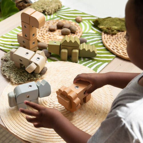 Een kind speelt met Guidecraft houten dieren bouwblokken op een tafel met rieten onderzetters.