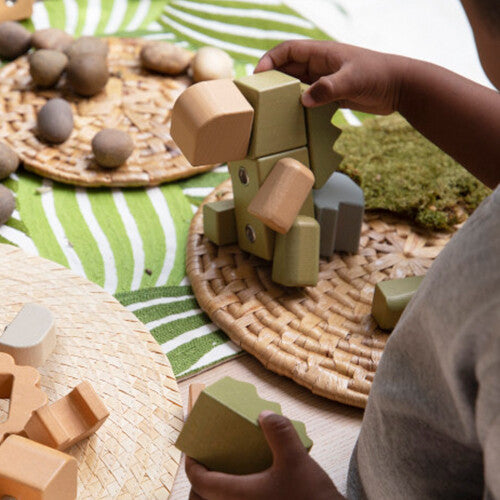 Kinderhanden bouwen een Guidecraft houten krokodil van bouwblokken op een rieten onderzetter.