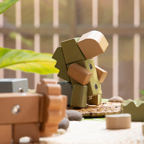 Een Guidecraft houten krokodil bouwblok staat op een houten ondergrond met planten op de achtergrond.