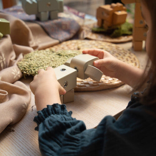 Kinderhanden spelen met een Guidecraft houten olifant bouwblok op een houten tafel.