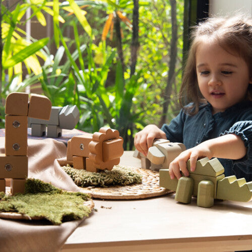 Een kind speelt met Guidecraft houten dieren bouwblokken op een tafel met planten op de achtergrond.