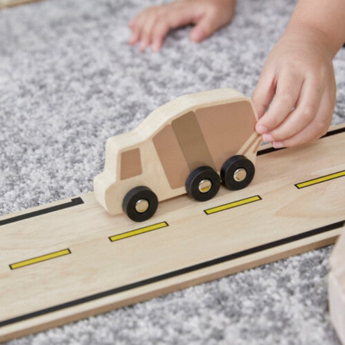 Een kinderhand duwt een houten cementwagen over een recht stuk van de houten autoweg.