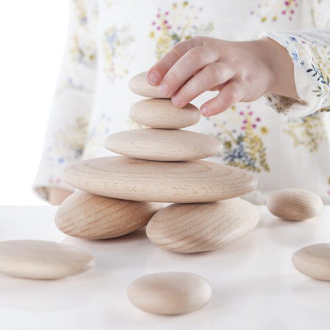 Een kinderhand stapelt een kleine houten riviersteen op een toren van houten stapelspeelgoed.