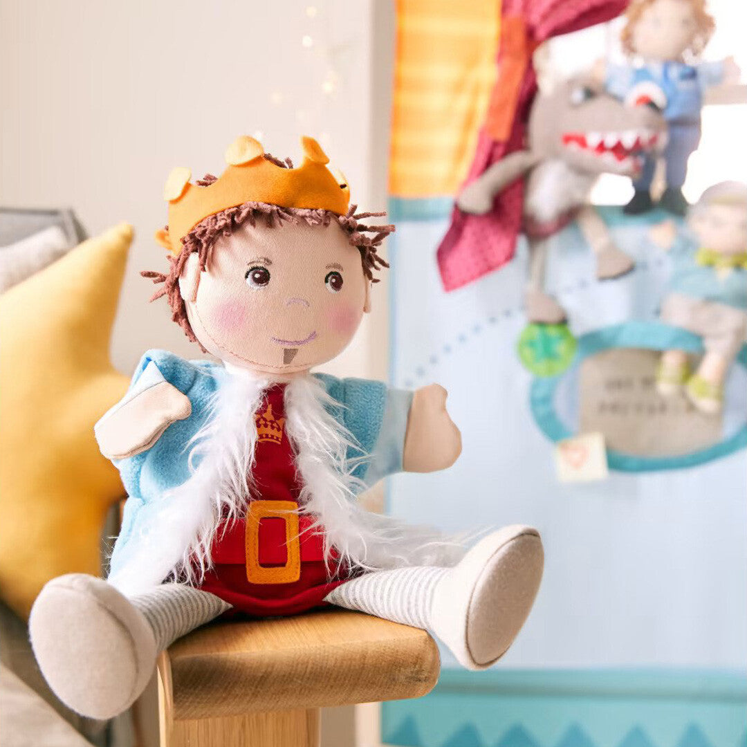 Haba handpop prins Emir zittend op een houten krukje met een poppenkast op de achtergrond.