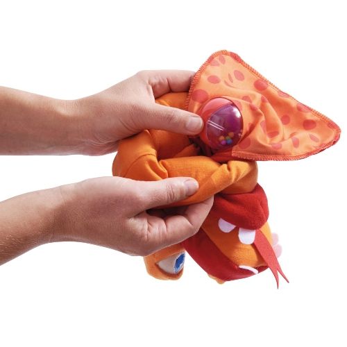 Twee handen vouwen de Haba handpop draak met rammelaar in elkaar.
