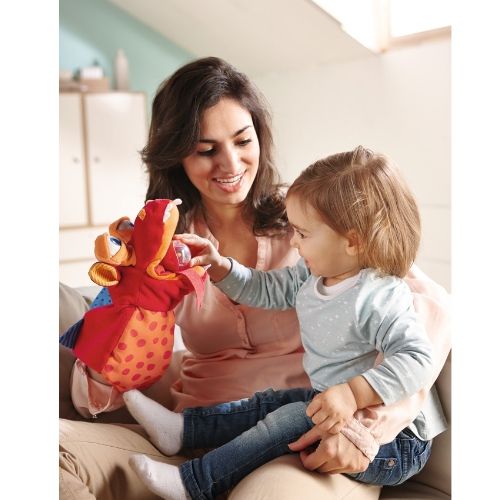 Een vrouw speelt met een Haba handpop draak voor een peuter op de bank.
