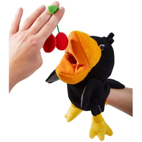 Haba handpop raaf kijkt met open snavel naar een hand die rode kersen vasthoudt.