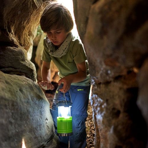 Kind met een brandende Haba groene campinglamp in een donkere grot.