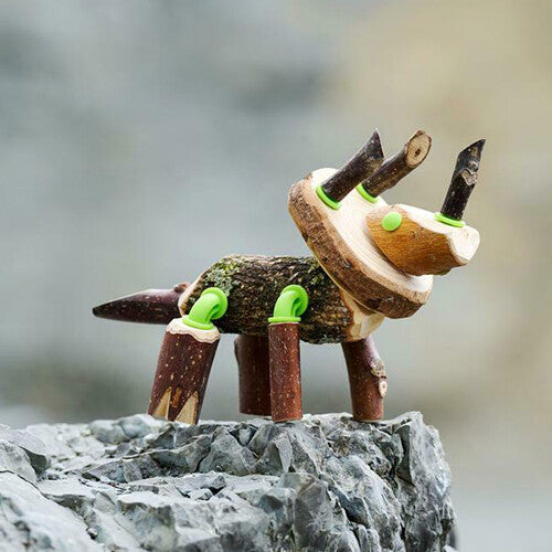 Een zelfgemaakte Triceratops dinosaurus van takken en groene connectors staat op een rots.